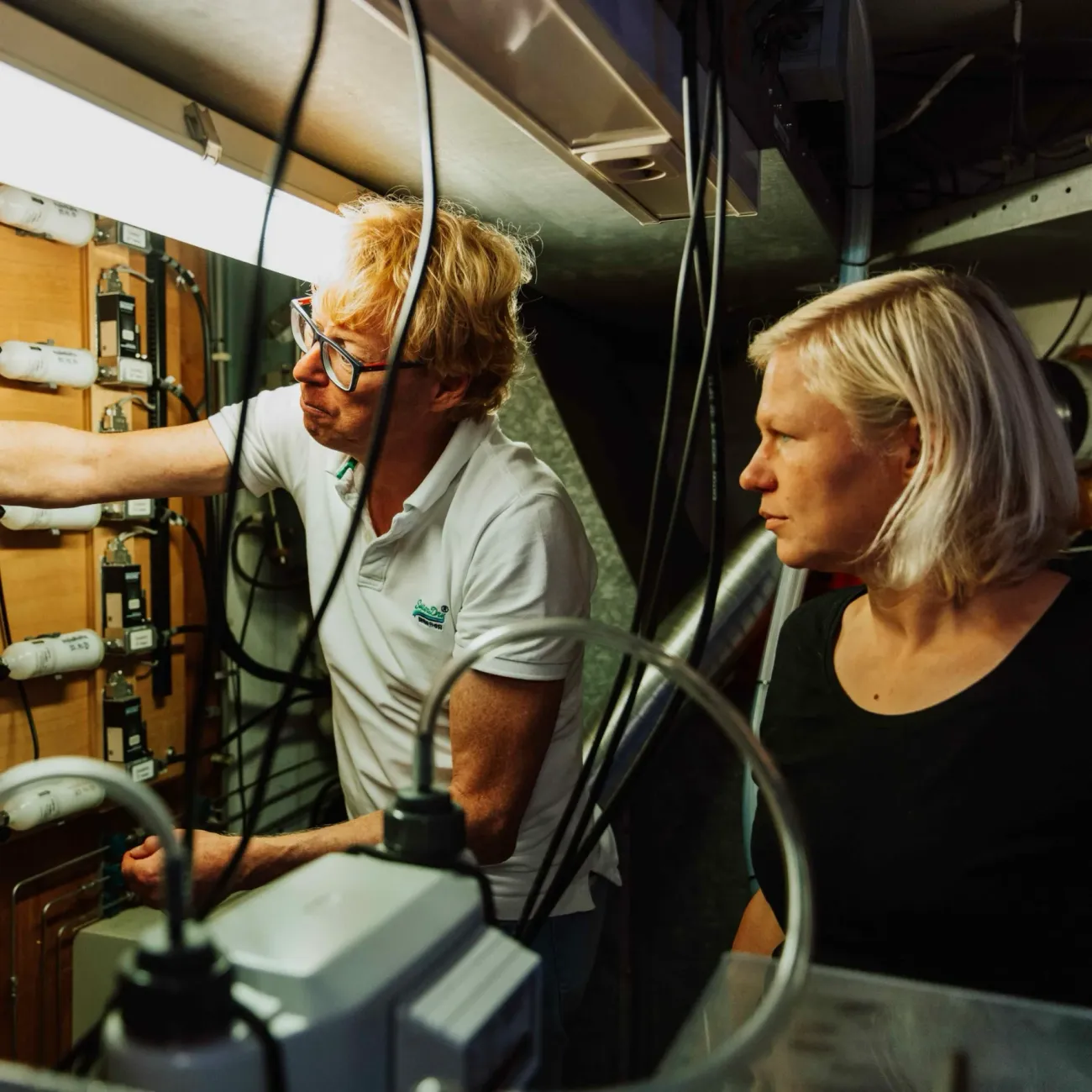 Two people standing next to each other are looking to the left at measuring instruments.