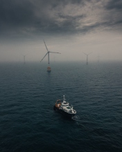 picture of a sea with a ship on the foreground and wind turbine on the background